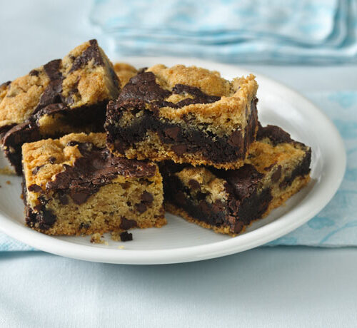 A white plate with several pieces of marbled chocolate chip cookie bars, placed on a blue patterned napkin.