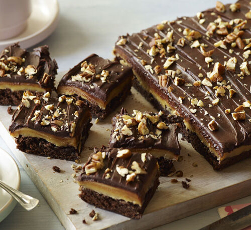 Chocolate caramel nut bars cut into squares on a board, with a cup of coffee on the side.