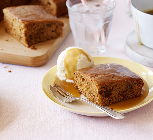 A plate with sticky toffee pudding, a scoop of vanilla ice cream, and caramel sauce, with a glass of water nearby.