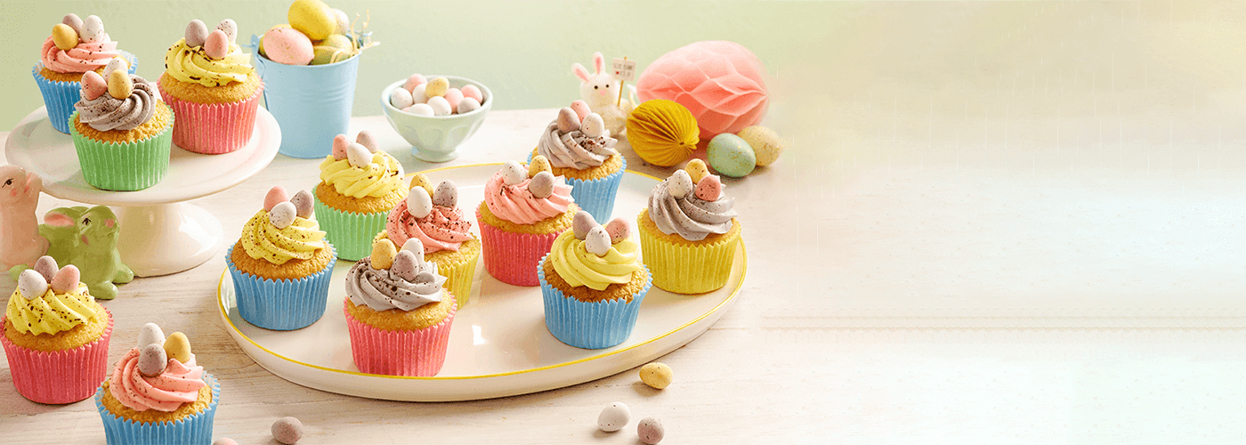 an assortment of vibrantly colored Speckled Mini Egg Cupcakes arranged on white platter, each topped with swirls of frosting
